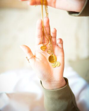 lot de 5 colliers contenant chacun au moins un pendentif, tous couleur or, gravés en lettre latines ou arabes, tenus en main et exposés