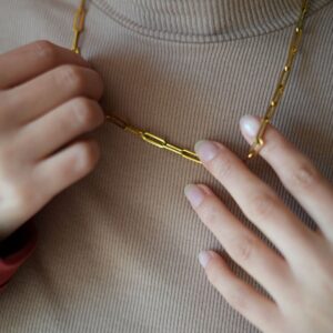 Collier en anneaux dorés porté au cou et tenus à deux mains
