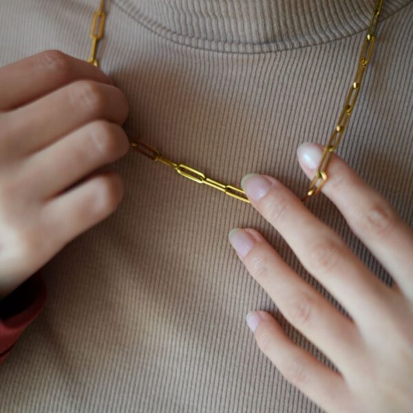 Collier en anneaux dorés porté au cou et tenus à deux mains