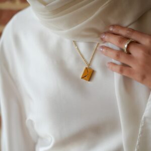 Mannequin vétu en blanc, portant un bijou enveloppe dorée