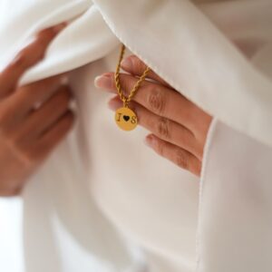Chaine en forme de corde et son pendentif portés sur voile blanc. acier doré
