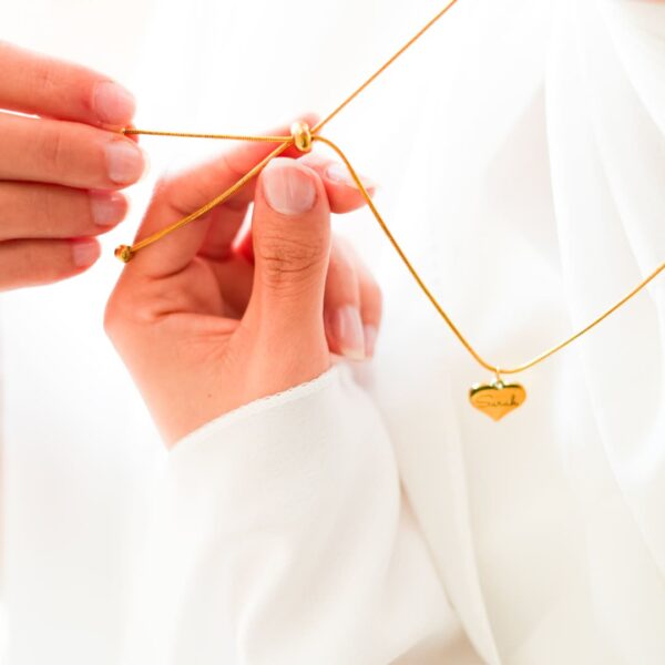un collier à fermeture coulissante tenu en mains par un mannequin vétu en blanc, avec un pendentif coeur en fond