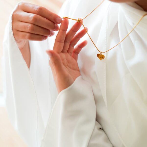 un collier à fermeture coulissante tenu en mains par un mannequin vétu en blanc avec médaillon en coeur gravé