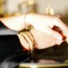 mains croisée, le mannequin arbore 3 bijoux au poignet droit, et deux à gauche (flouté). Tous dorés