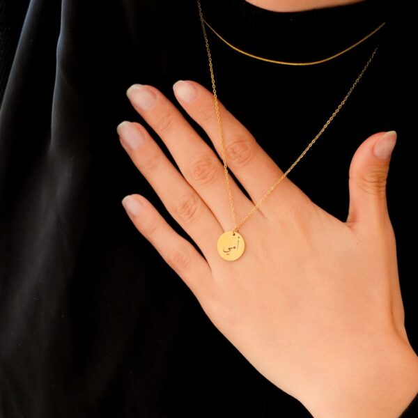 Collier Ummi gravé sur un petit disque, porté et tenu à une main