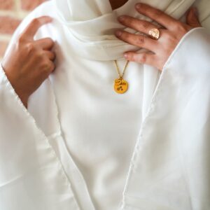 Une chaine, deux pendentifs, sur un mannequin vétu en blanc. Le bijou personnalisé sort de sous un voile blanc