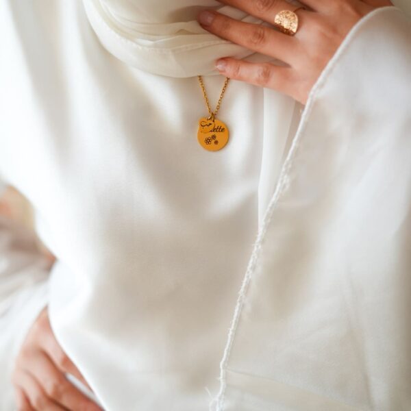 Une chaine, deux pendentifs gravé en noir, sur un mannequin vétu en blanc