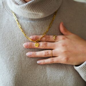 Bijou personnalisé en anneau porté au cou, sur pull col roulé, et son pendentif. Main avec bagues