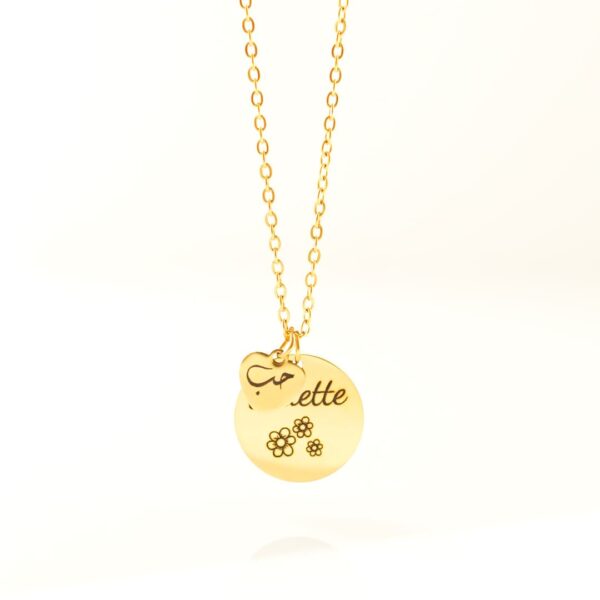 Bijou en acier personnalisé avec deux pendentifs : un gros disque gravé avec 3 petites fleurs et un petit coeur sur lequel est gravé Hubb - Amour en arabe