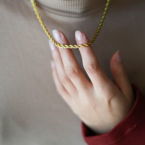 Collier doré torsadé porté au cou, tenu en main